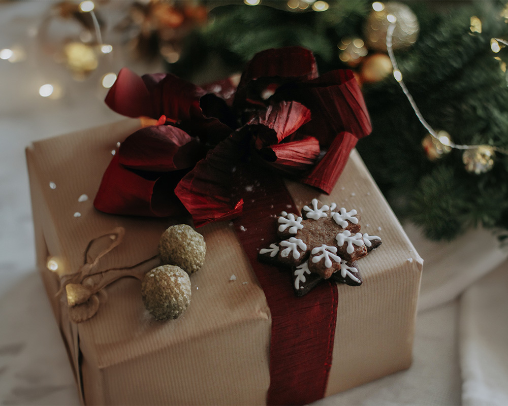 Ziemassvētku dāvana ietīta papīrā, sasieta ar loku un dekorēta ar cepumu.