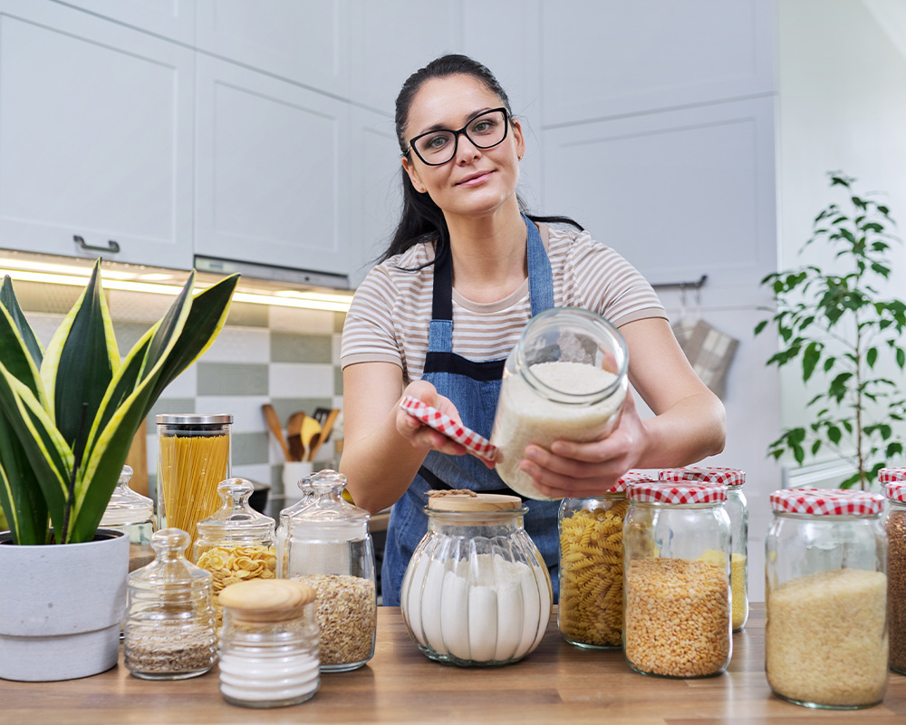 Sieviete virtuvē rāda burciņas sauso pārtikas produktu uzglabāšanai