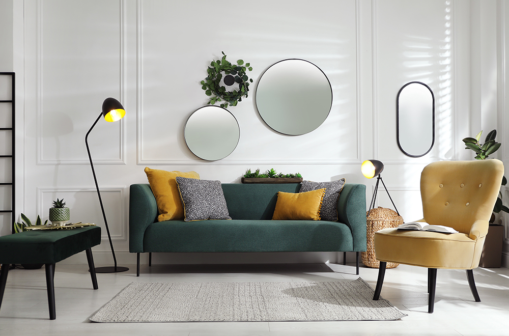 Mūsdienīga viesistaba gaišās krāsās ar zaļu dīvānu, dzelteniem spilveniem un apaļiem spoguļiem uz sienas.
