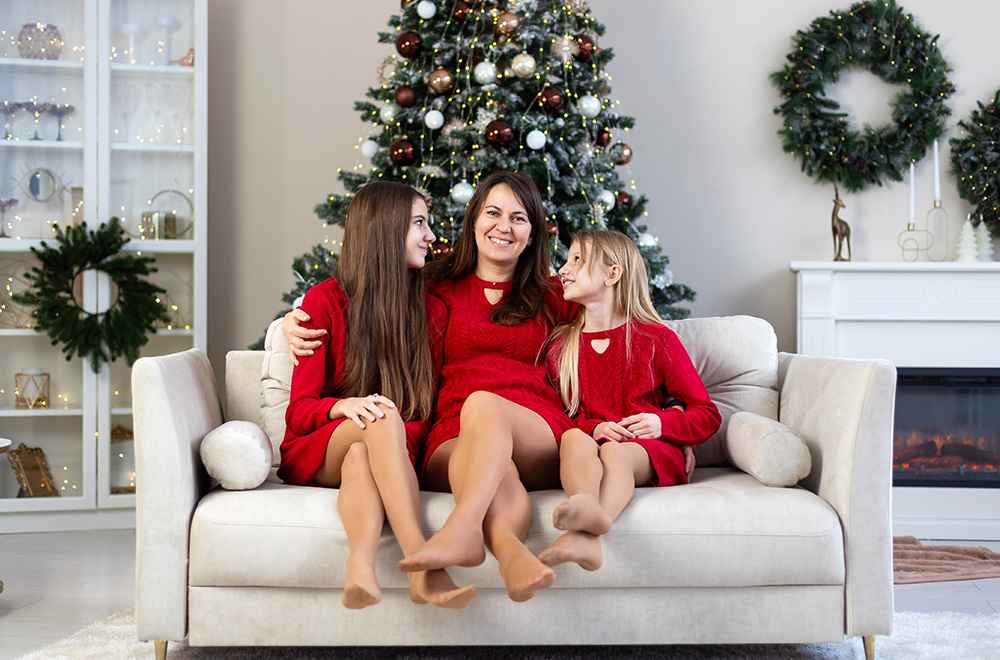 Māte un viņas meitas sarkanās kleitās kopā pavada svētku laiku pie Ziemassvētku eglītes.