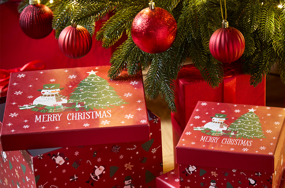 Dāvanu kastītes ar Ziemassvētku motīviem blakus Ziemassvētku eglītei.