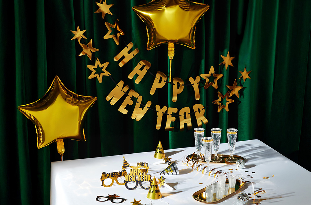 Galda dekors Jaunā gada svinībām, ar baloniem, glāzēm un zelta rotājumiem.