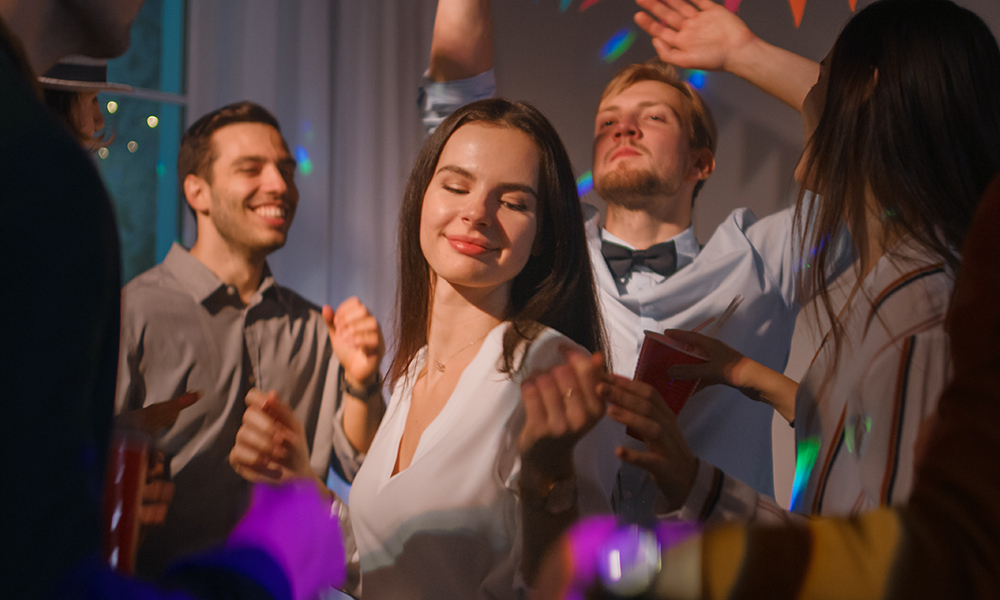 Cilvēku grupa dejo ballītē, starp viņiem ir sieviete, kas bauda mūziku.