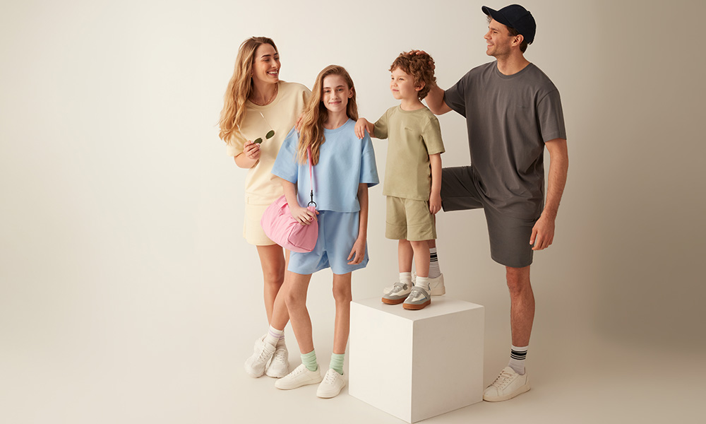 Ģimene pasteļtoņu apģērbā kopā pozē uz gaiša fona.